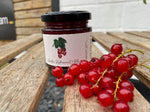 Jar of redcurrant jelly with a branch of redcurrants on a wooden surface
