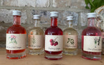 Five small bottles of different types of vinegar on a wooden surface with a stone wall background.